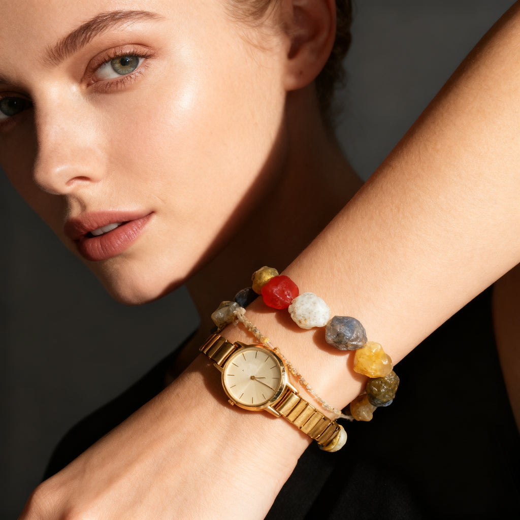 Natural agate bracelet stacked with a slim gold watch on a wrist, dark editorial tone