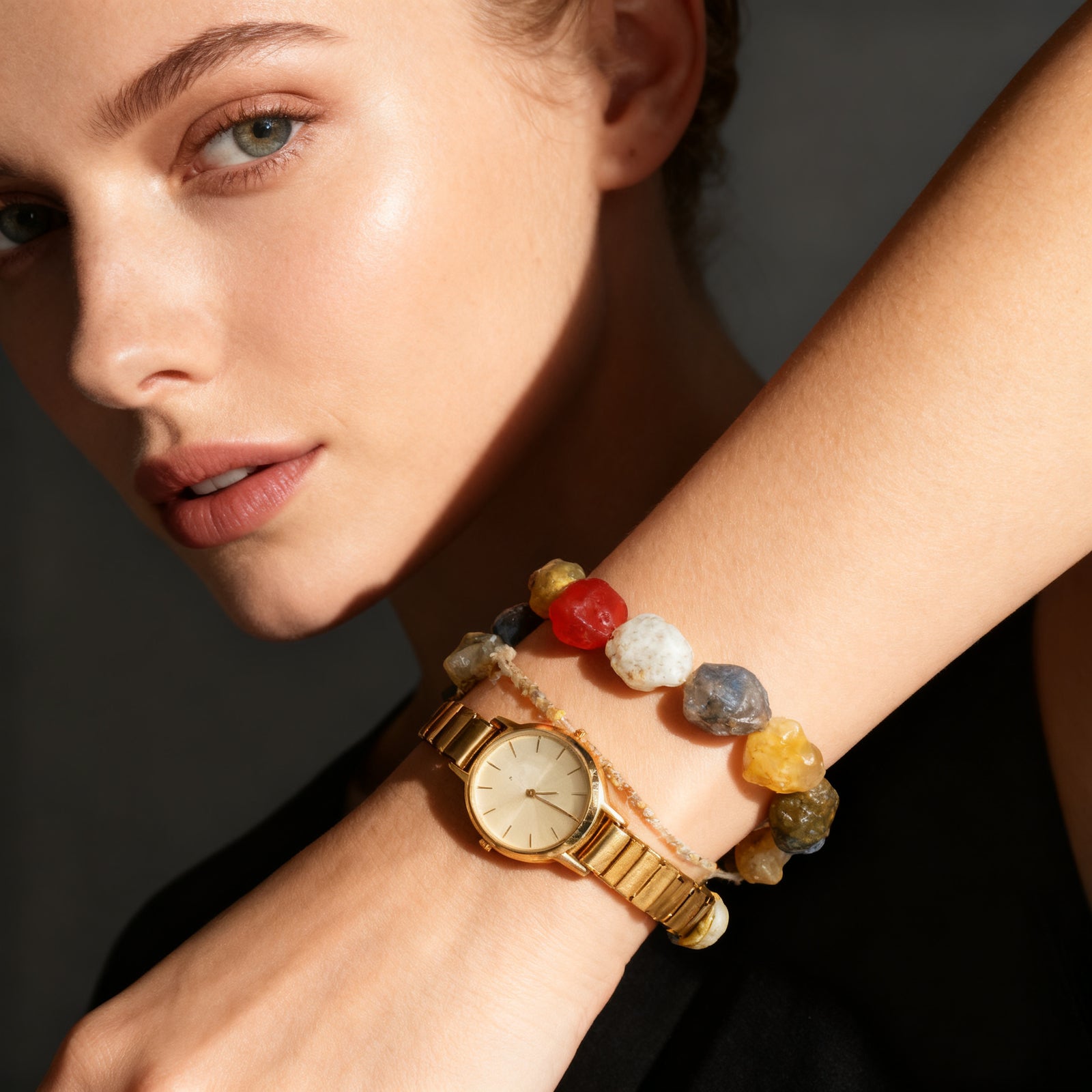 Natural agate bracelet stacked with a slim gold watch on a wrist, dark editorial tone