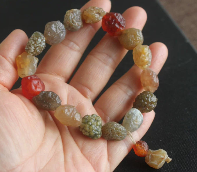 Natural Alxa colorful agate raw stone handcrafted bracelet held in hand showing red yellow brown cream gray beads